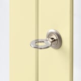 Detailný záber na sklenené dvere skrinky krémovej farby s otvoreným kruhovým zámkom so striebornou rukoväťou.