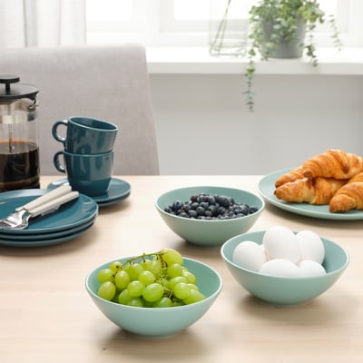 Stôl so svetlomodrými miskami ovocia a croissantov, naskladanými šálkami a french pressom, pripravený na raňajky.