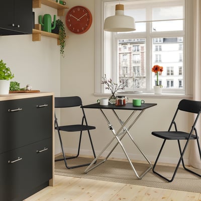 Moderný kuchynský kútik s čiernym stolom GUNDE , červenými hodinami, zelenými akcentmi a veľkým oknom.