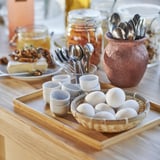 Malé porcelánové poháre na vajíčka v košíku na stole, ideálne na raňajky, jednoduchý a odolný dizajn.