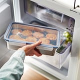 Osoba, ktorá vkladá priehľadnú nádobu s potravinami do chladničky, utesnenú nepriepustným vekom pre čerstvosť.