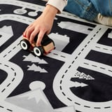 Detské ručne riadené drevené auto na čiernobielom hracom koberci s mestským a lesným vzorom.