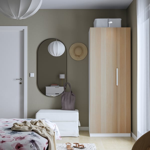 Minimalistická spálňa so skriňou PAX zo svetlého dreva, bielymi zásuvkami a okrúhlym zrkadlom. Šatník je vysoký a štíhly.