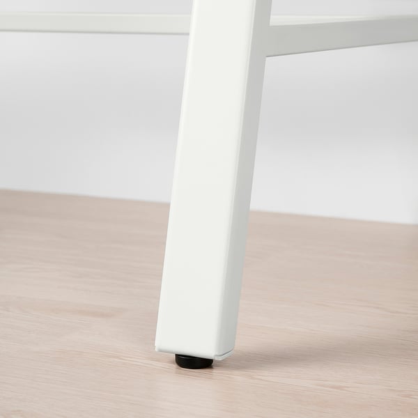 Detailný záber na bielu nastaviteľnú nohu stola s čiernym chráničom podlahy na svetlej drevenej podlahe.