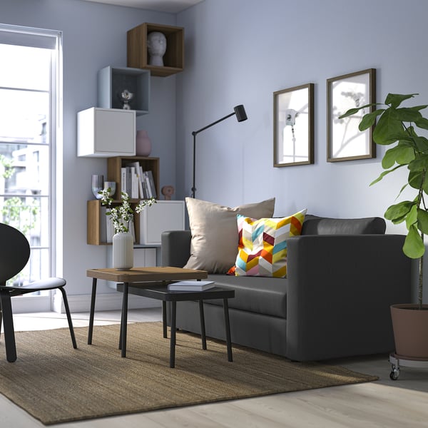 Moderná obývacia izba so sivou rozkladacou pohovkou, farebnými vankúšmi, dreveným konferenčným stolíkom a rastlinami.