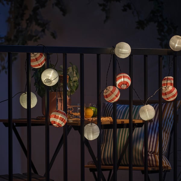 Balkón osvetlený solárnymi lampášmi, ktoré vytvárajú atmosférické svetlo. Lampáše visia zo zábradlia a poskytujú dekoratívnu žiaru.