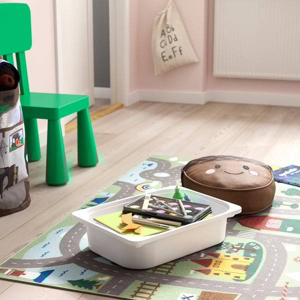 Farebná detská herňa so zelenou stoličkou, plyšovou hračkou, vankúšom so smajlíkom a úložným košom TROFAST plným puzzle na tematickom koberci.