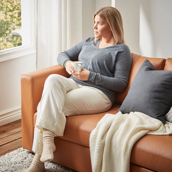 Žena relaxuje na pohovke VIMLE s kávou, dekou a slnečným žiarením.