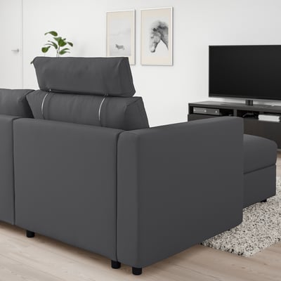 Šedá sekcionálna pohovka VIMLE v minimalistickej obývacej izbe s TV a umením.