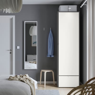 Vysoká biela skrinka VISTHUS s elegantným, moderným dizajnom. Stojí na nastaviteľných nožičkách a jednej zásuvke a dvoch dverách.