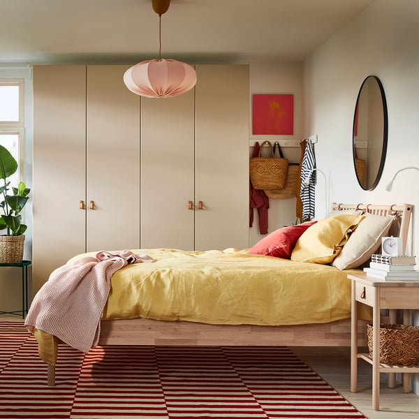 Bright bedroom with yellow bed, red rug, crafted wood furniture, hanging lamp, wall mirror, and artwork.