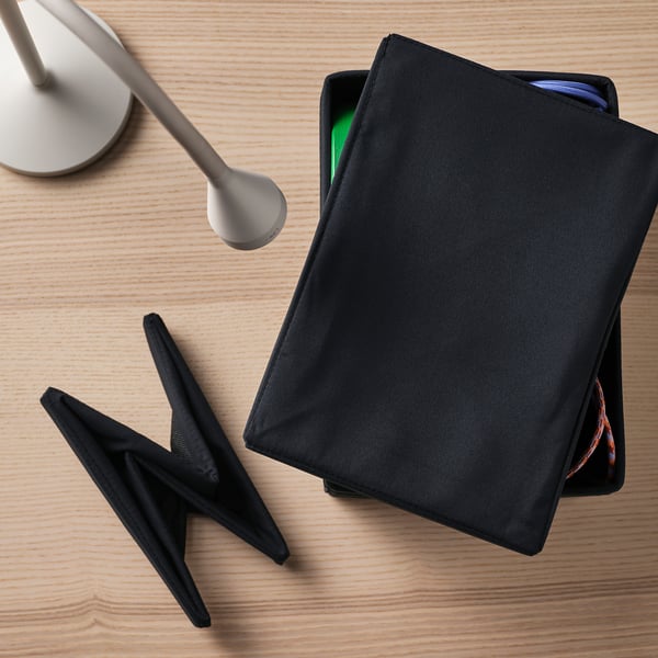 Black fabric storage box with lid and handles on wooden desk next to lamp.