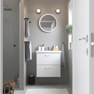 Modern bathroom with ENHET white cabinet, featuring round mirror, grey walls, and glass shower. Compact yet spacious design.