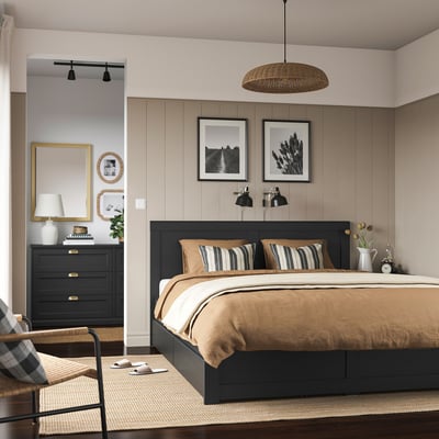 Black FÅGELFJÄLLET bed with beige linens, nightlights, black dresser, mirror, armchair.