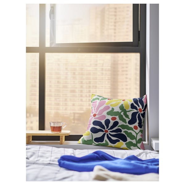 Bright pillow with floral design rests on bed by window, blue blanket nearby.