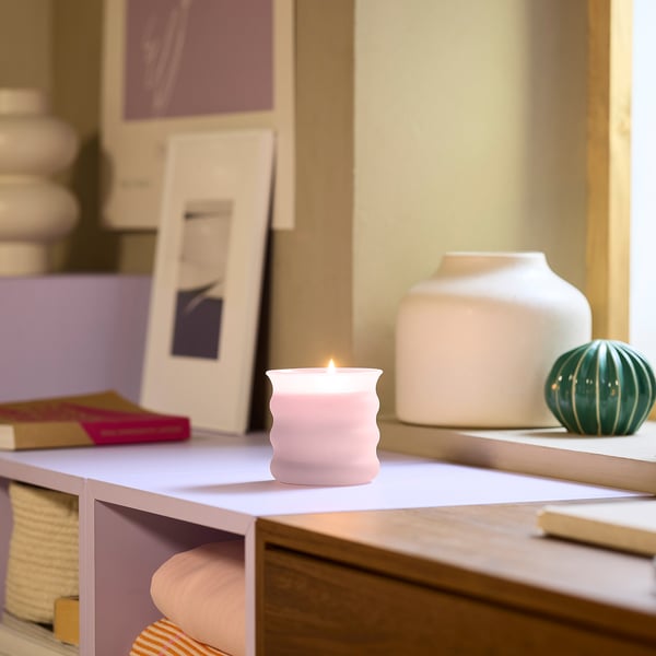 JUVELTRAST candle: pink, glass, round, lit. Small beside vases on shelf.