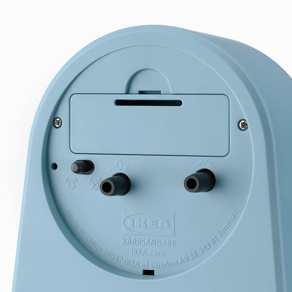 Back of light blue IKEA alarm clock with two knobs, tiny bell icon, and labels.