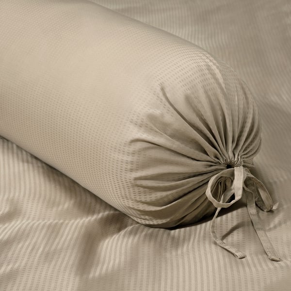 Beige bolster pillow with drawstring cover on striped bedsheet.