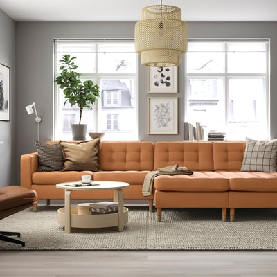 Modern living room with large orange l-shaped sofa, round coffee table, and leafy plant. The sofas big and comfy, taking up most of the space.