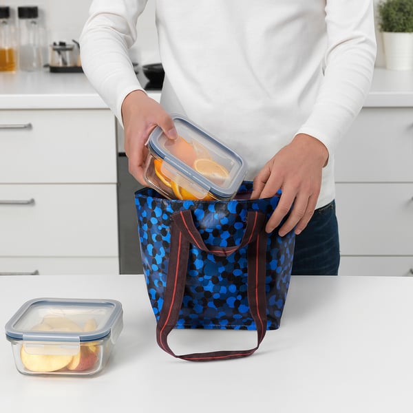 Person placing food containers into a blue polka-dot cooler bag on a kitchen counter.