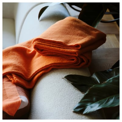 A bright orange folded wool blanket, STOCKHOLM 2025, made with 50% merino wool, showcasing soft texture and warm design.