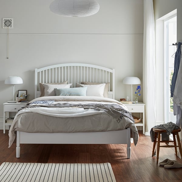 Bedroom with TYSSEDAL white bed, striped blanket, matching rug, two lamps, and wooden floor.