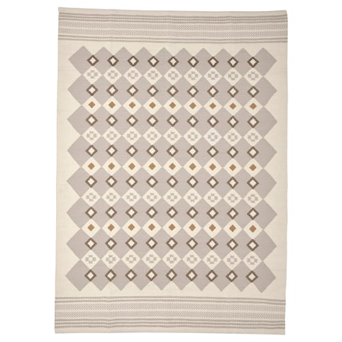 The VÄGNÄT rug in neutral grey and cream, featuring a traditional diamond pattern with handmade, intricate designs and wool material.