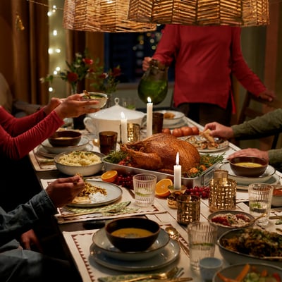 A cozy dinner table with a roasted turkey centerpiece, surrounded by side dishes and people serving food in warm candlelight.