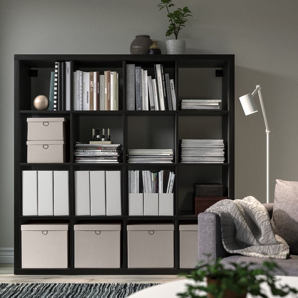 Black KALLAX bookshelf with shelves, chair, and lamp.