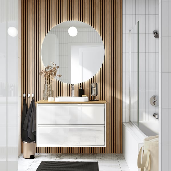 Modern white bathroom vanity with marble basin, wooden wall, mirror, and shower.