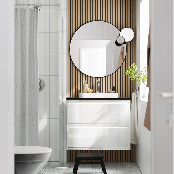 Modern bathroom ÄNGSJÖN vanity with marble basin, wooden panels, round mirror, & shower curtain.