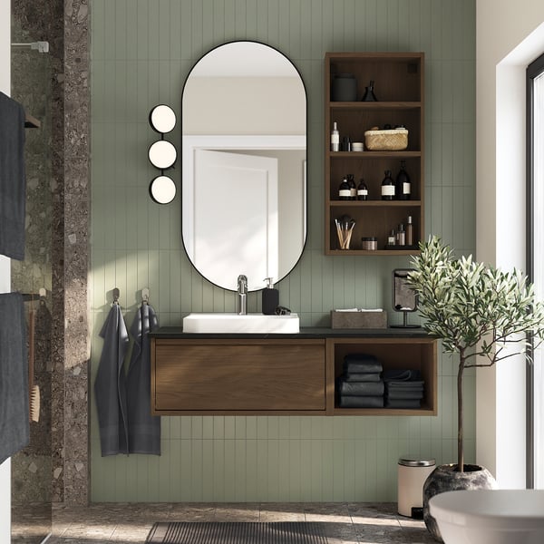 Modern green bathroom with dark wood ÄNGSJÖN vanity, sink, mirror, shelves, plant, and minimalist handles.
