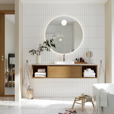 Minimalist bathroom with round mirror, light wood drawers, greenery, open design.