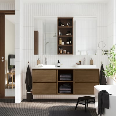 Modern bathroom with wooden cabinets, white countertops, open shelves, and a freestanding tub. Dark towels hang nearby.