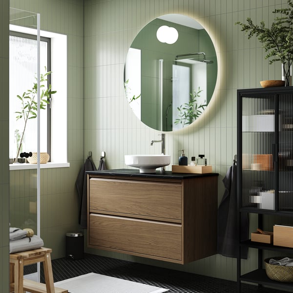 Modern bathroom with ÄNGSJÖN vanity, mirror, & sink. Dual drawers under window, black accents.