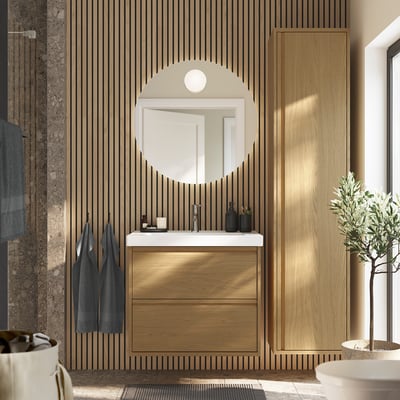 Modern bathroom with oak vanity, mirror, plant. Minimalist drawers, sleek sink, hanging towels.