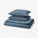 Folded blue cotton bedding set, including duvet cover and pillows. Soft, casual, and square-shaped.
