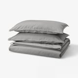 Grey folded bedding set, including duvet and pillows, neatly stacked. Soft cotton material with casual design.