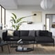 Modern living room a dark grey ÄPPLARYD sofa with grey and beige pillows, a black coffee table, and a large green plant.