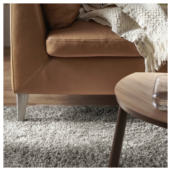 A cosy living room setup with a brown leather sofa, a light-colored shaggy rug, and a round wooden coffee table.