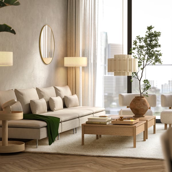 Modern living room with white rug, cream sofa, wooden table, city view windows, green throw.