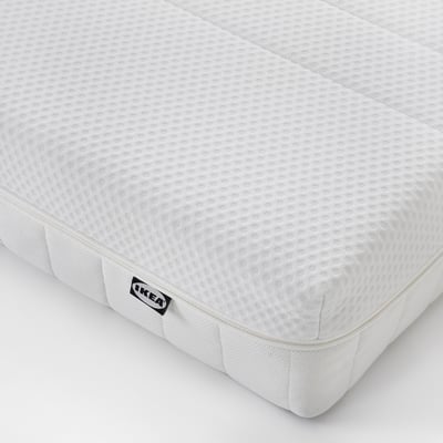 Close-up of white ÅKREHAMN mattress, showing its firm, textured surface and a small black IKEA tag on the corner.