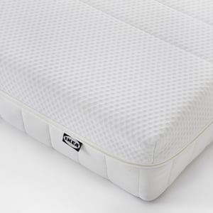 A corner of a firm memory foam mattress by IKEA, showing clean white, quilted fabric and a branded tag.