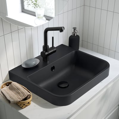 Black semi-recessed washbasin on countertop with modern tap, soap dispenser, and towel basket.