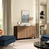 Modern living room with BESTÅ brown sideboard, books, flowers, lamp, blue sofa, and home office area.
