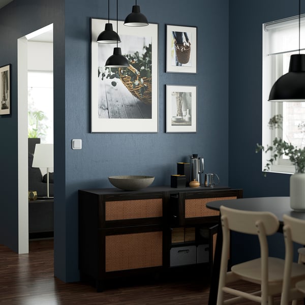 Modern living room with blue walls, white chairs, black sideboard with woven baskets, and framed photos on the wall.