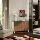 Modern living room with BESTÅ light brown wooden sideboard, white lamp, abstract art, and white sofa on patterned rug.