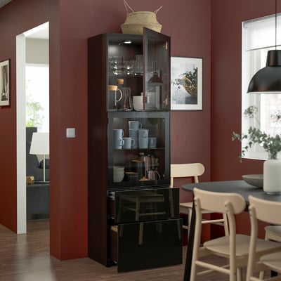 Dark wooden display cabinet with glass doors and shelves, showing cups and vases. Positioned in a dining area with red walls and white chairs.
