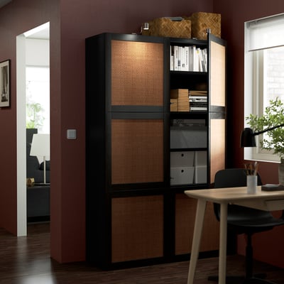 Black wooden storage unit with brown wicker front panels. It has sliding doors and adjustable shelves, positioned in a home office setting.