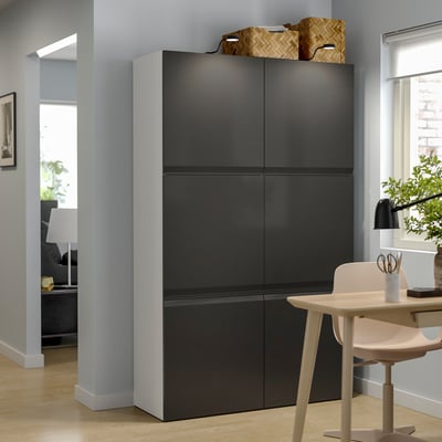 Modern living space with tall black BESTÅ storage unit. Topped with woven baskets, accompanied by a light wood desk and white chair.